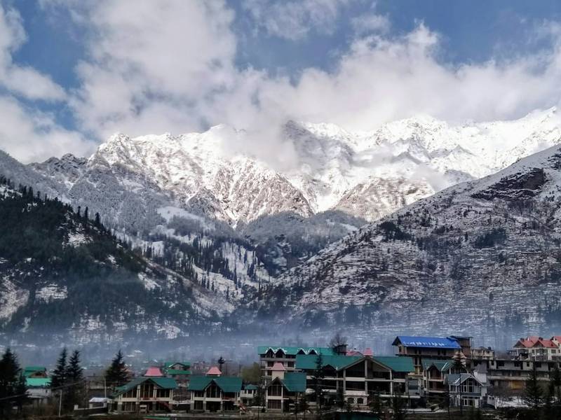Town with green roofs below snow-covered peaks in Manali